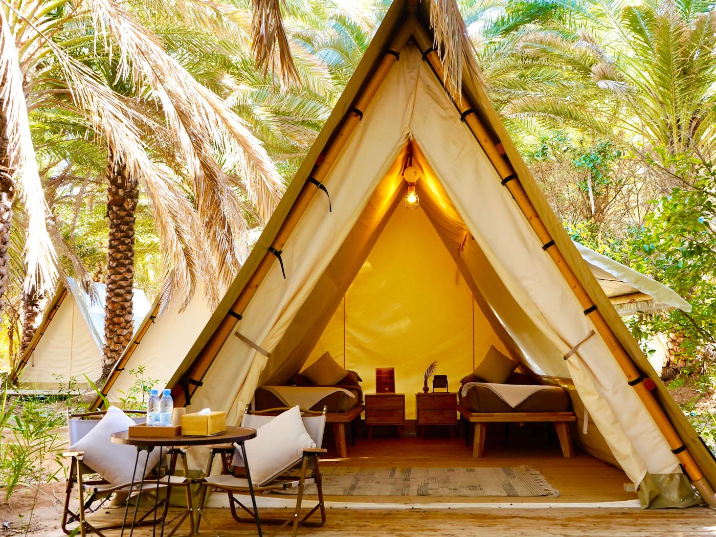 A glamping tent under the palms at Husaak Centre AlUla, with two beds and a seating area